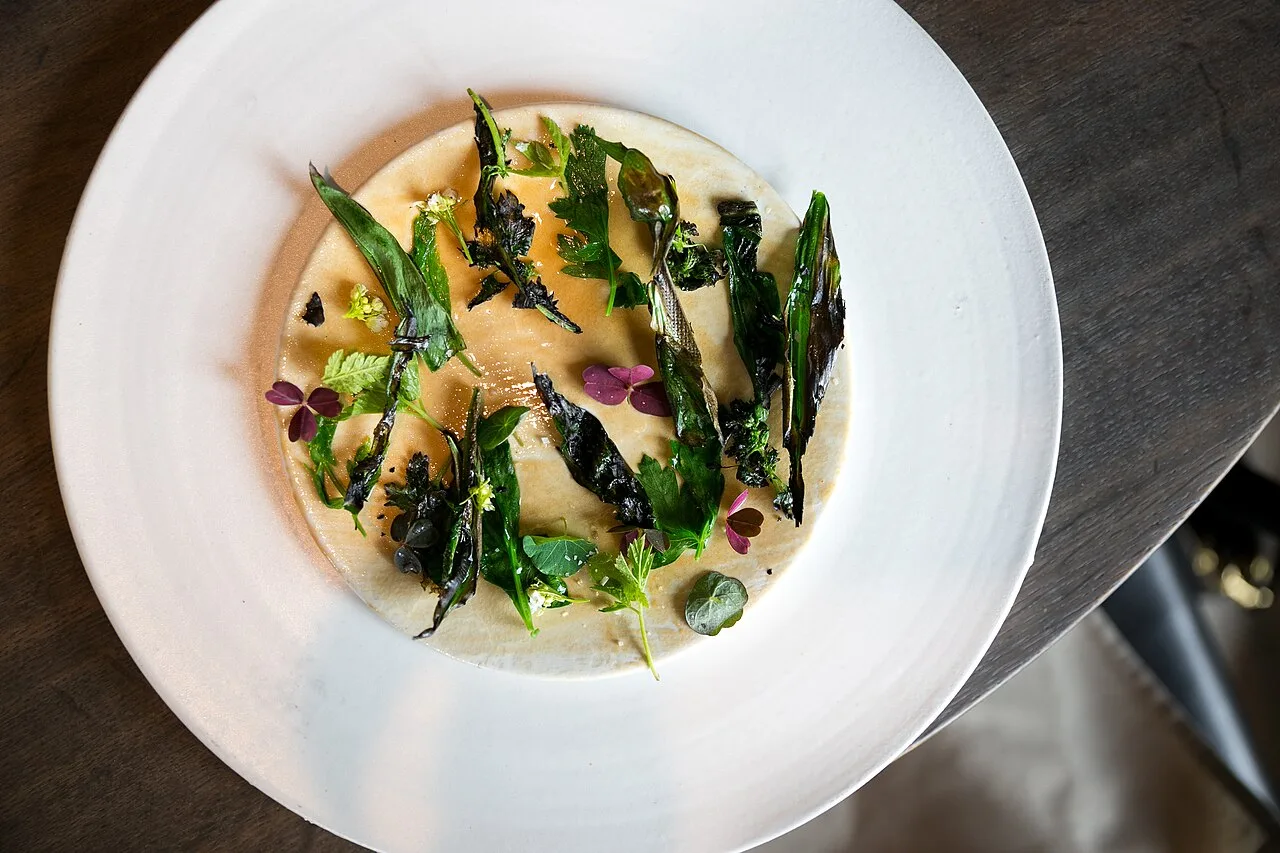 Fine-dining plated course of grilled and fresh greens over scallop paste